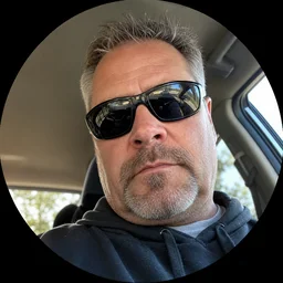 A man in sunglasses looking down at the camera from inside a car